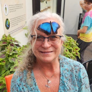 Photo of Andie with a blue morpho butterfly resting on her forhead.